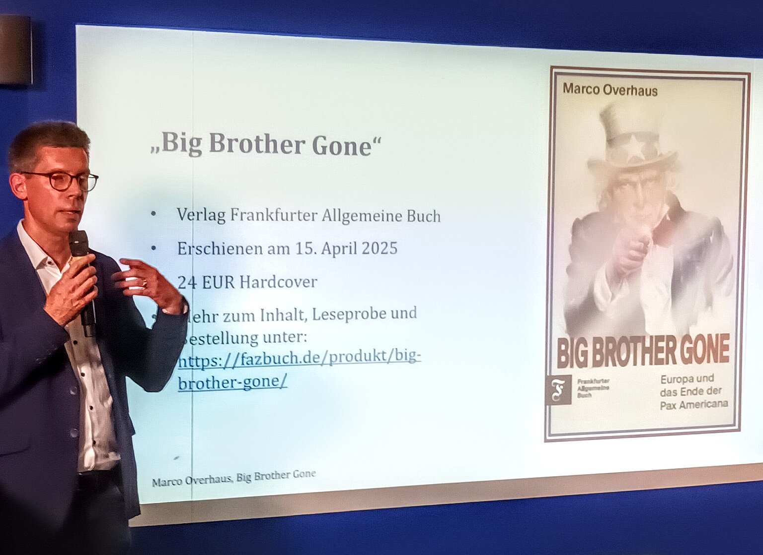 Autor steht vor Leinwand mit eingeblendetem Buchtitel – 